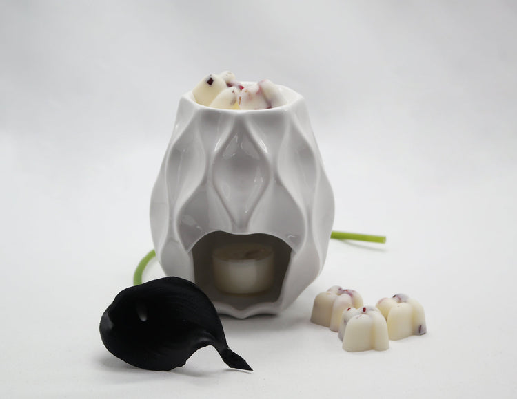 White Nico wax burner with ripple effect and well filled with rose petal infused wax melts and a black lily placed beside it