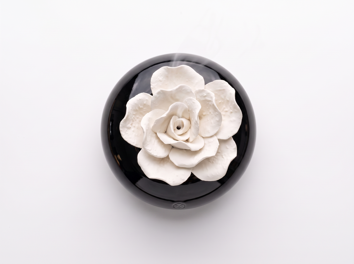 A round black object with a raised white flower design on top, photographed from above on a plain white background.