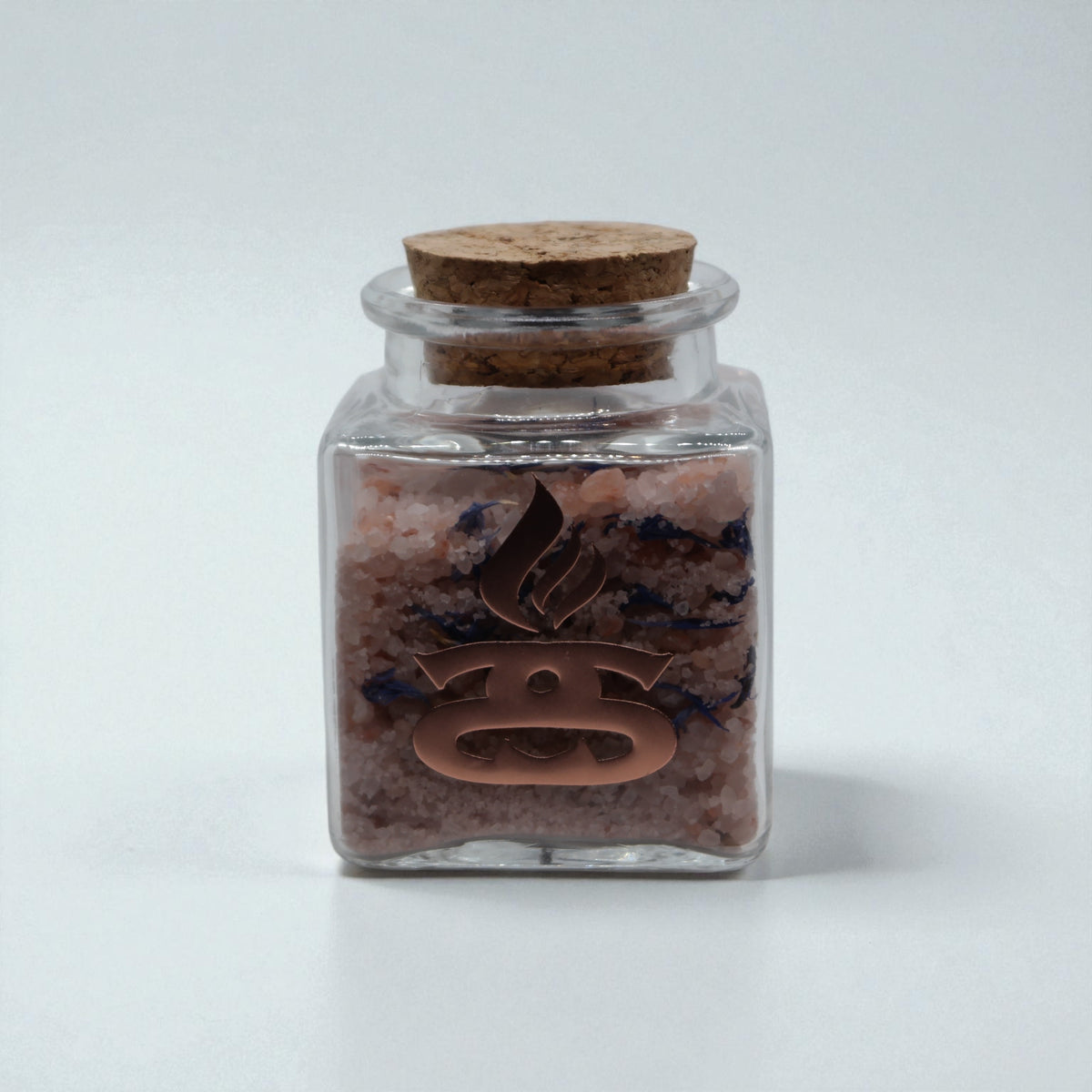 Lavender, Lemon and Geranium Simple Scents Minis Essential Oil Bath Salts and Foot Soak - 50g small square clear glass jar with cork stopper filled with pink bath salts and dark lavender botanical flakes, Simple Scents rose gold logo on front, front view on light grey background