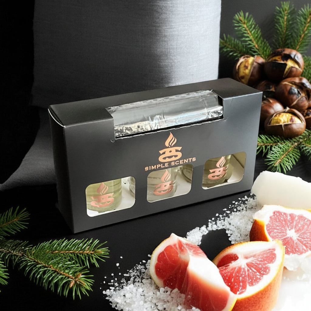 Simple Scents Excellence Reed Diffuser Trio Fresh - black gift box with rose gold Simple Scents logo and three diffuser bottle windows, styled with pine branches, open conker shells, sea salt crystals and pink grapefruit slices on dark background