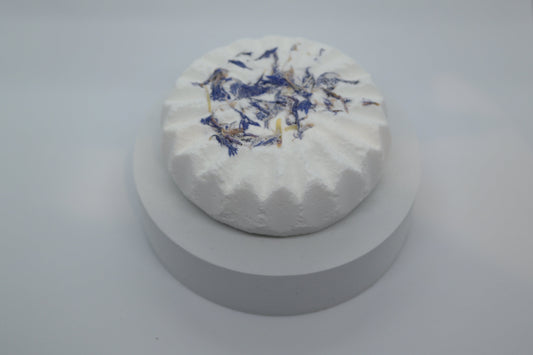 Simple Scents Aromatherapy Lavender & Frankincense Bath Bomb with dried blue cornflower petals, displayed on a white round plinth against a light grey background