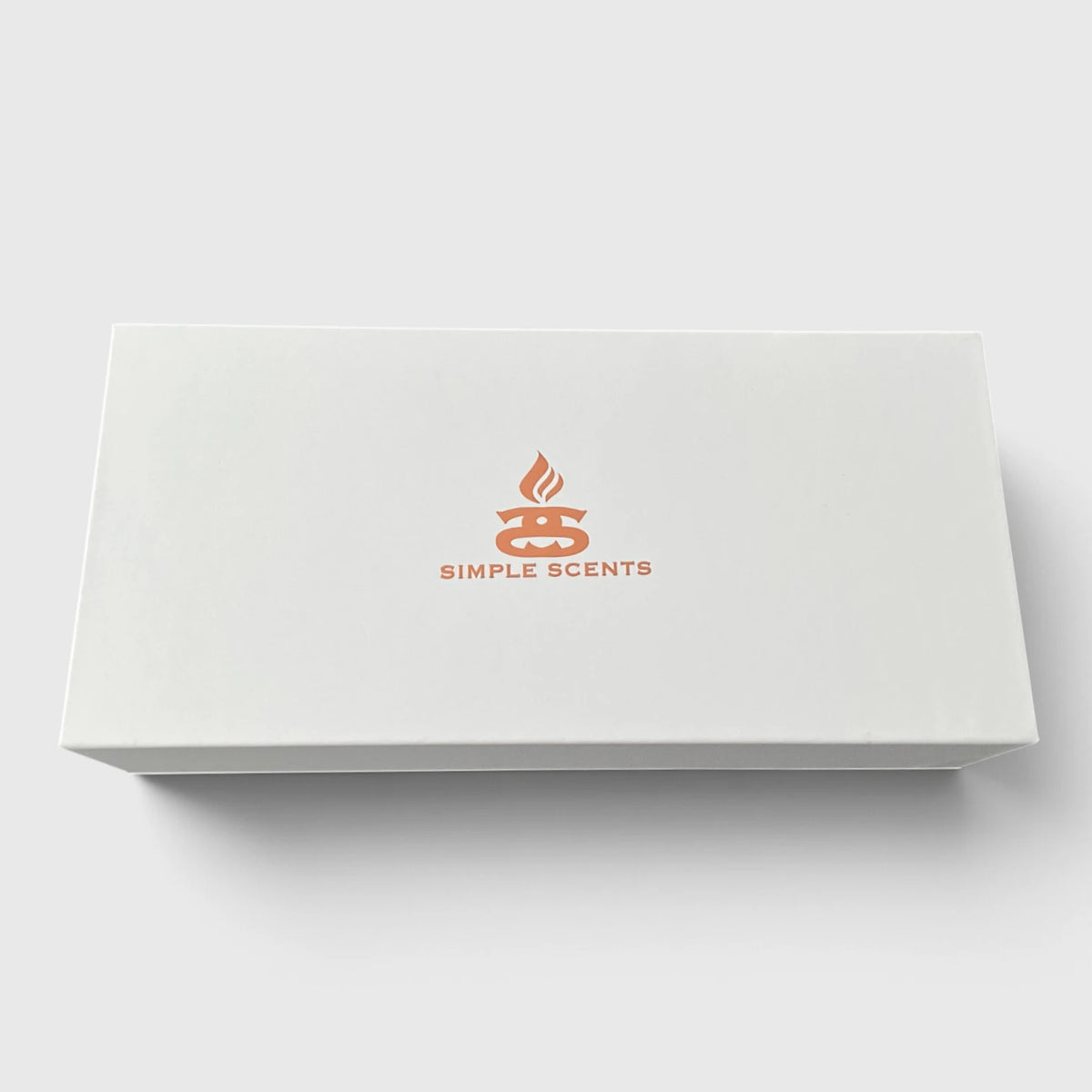 A white rectangular product box with a simple orange logo and the text 'SIMPLE SCENTS' centered on the lid, photographed on a light gray background.