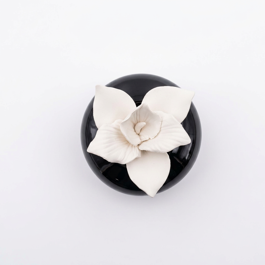 Overhead view of a white orchid flower aroma stone diffuser in a glossy black ceramic base.