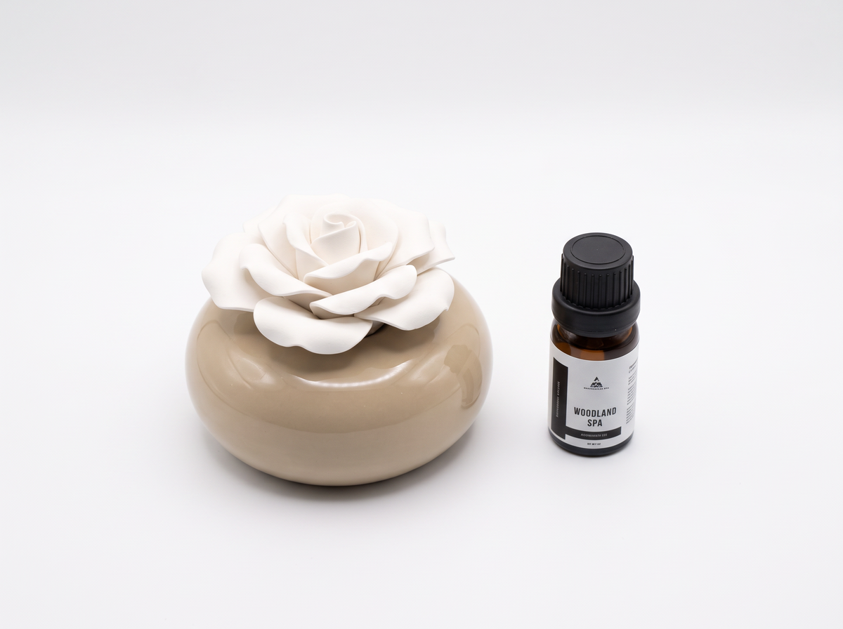 A small amber glass bottle with a black cap and white label next to a beige ceramic diffuser bowl with a white rose stone diffuser, on a clean white background.