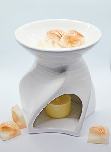 Lyon Ceramic Tea Light Wax Burner - gloss white twisted spiral Lyon ceramic wax burner with cream soy wax melt pieces in dish and lit tea light candle inside, with wax melt pieces scattered beside it on light blue background