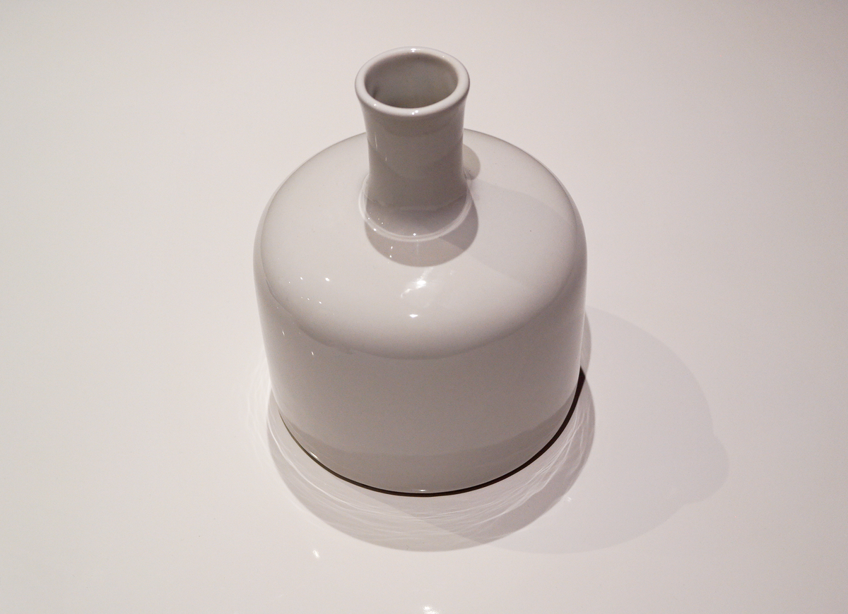 Angled view of the gloss-white Riley ceramic vase with a cylindrical neck and rounded body on a pale surface.