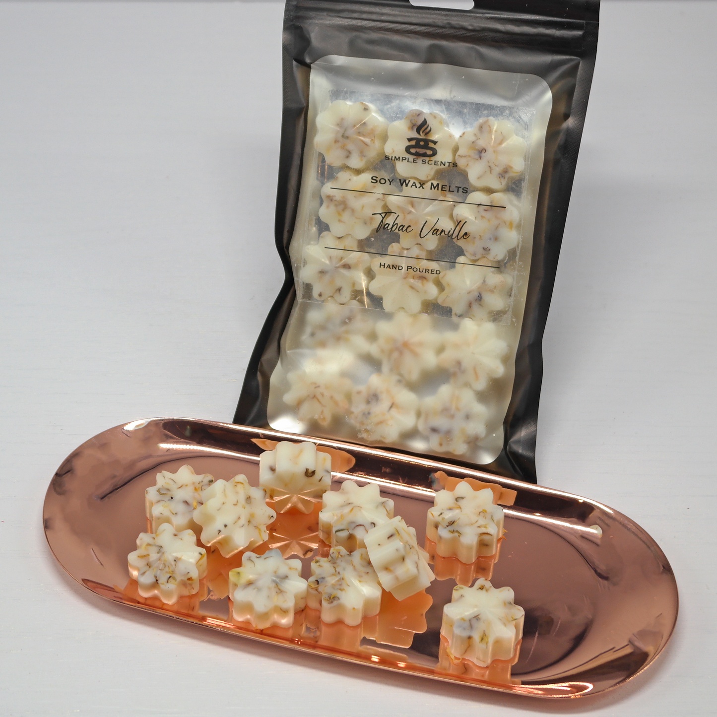 Tabac Vanille Simple Scents Ambience Mini Floret Style Wax Melts - cream and caramel shimmer floret-shaped soy wax melts on rose gold tray displayed in front of Simple Scents Soy Wax Melts Tabac Vanille resealable black packaging