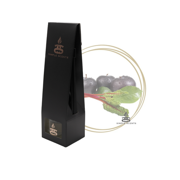 Black Plum and Rhubarb Simple Scents Excellence Reed Diffuser - matte black tall tapered packaging box with rose gold Simple Scents logo, displayed in front of black plums and rhubarb stalks inside a gold double-ring circle frame on white background