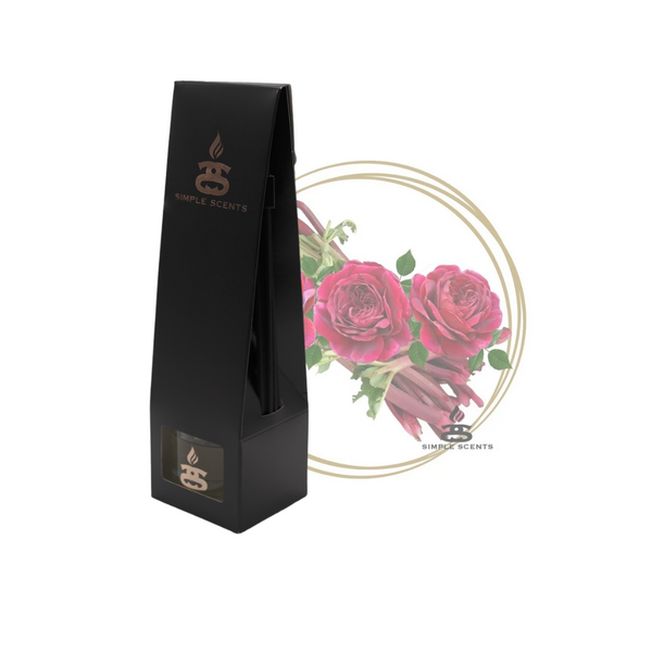 Rhubarb and Rose Simple Scents Excellence Reed Diffuser - matte black tall tapered packaging box with rose gold Simple Scents logo, displayed in front of deep pink roses and rhubarb stalks inside a gold double-ring circle frame on white background