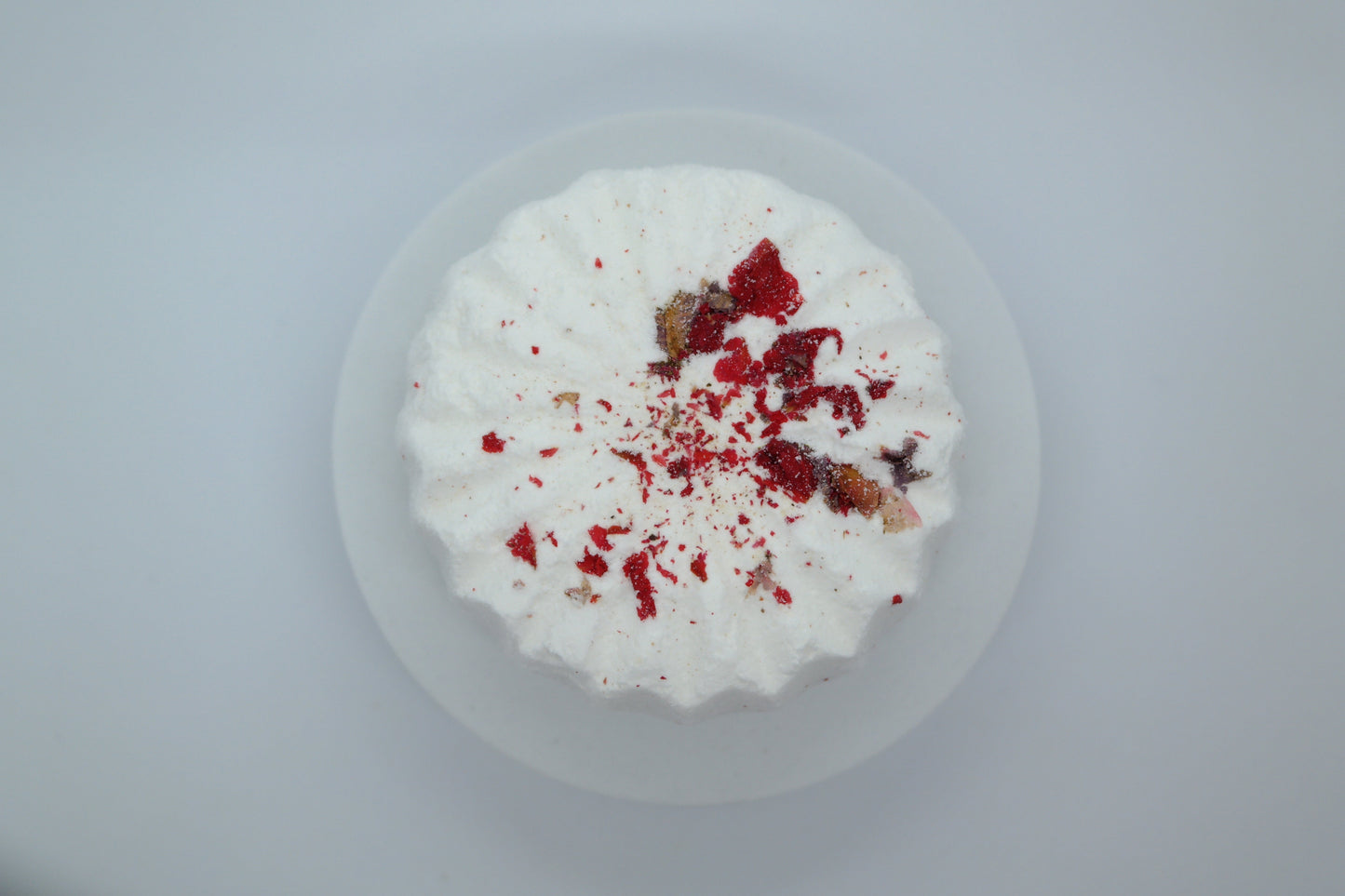 Simple Scents Aromatherapy Eucalyptus & Peppermint Bath Bomb with dried botanicals and red pomegranate flower petals on top, viewed from above on a light grey background