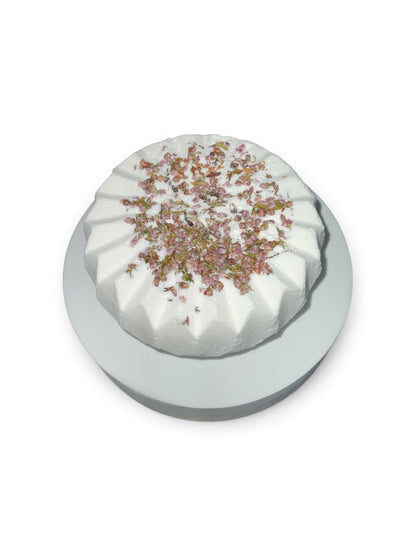 Simple Scents Tea Tree and Rosemary Aromatherapy Bath Bomb with dried heather floral botanicals on top, displayed on a white pedestal against a white background