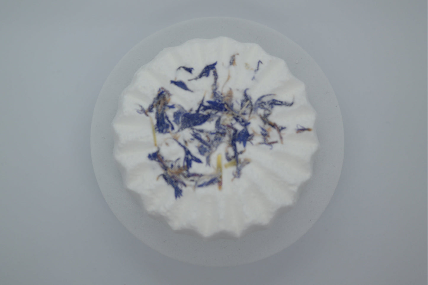 Simple Scents Aromatherapy Lavender & Frankincense Bath Bomb topped with dried blue cornflower petals, viewed from above on a light grey background
