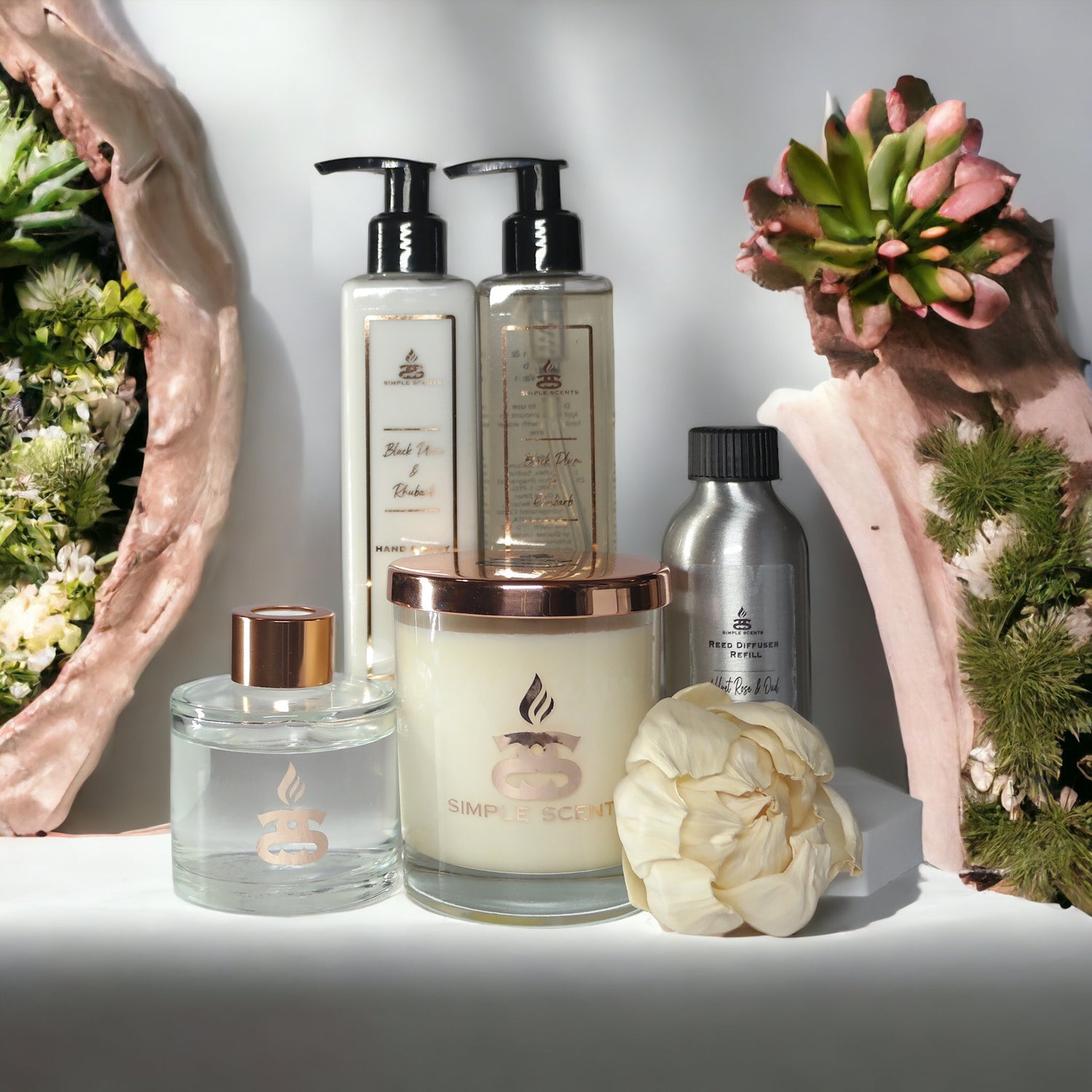 Picture of candle and Reed diffuser in a glass bottle with peony flower and two bottles containing a soap and lotion