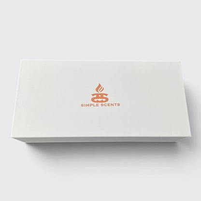 A white rectangular product box with a simple orange logo and the text 'SIMPLE SCENTS' centered on the lid, photographed on a light gray background.