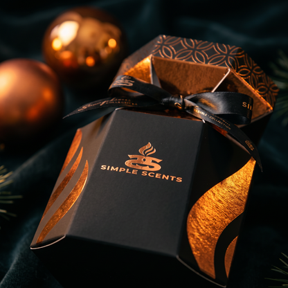 A black and metallic gold gift box for Simple Scents, tied with a black ribbon, set against a dark velvet background with gold holiday ornaments.