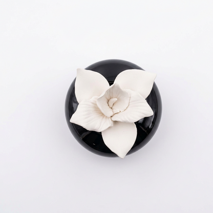 Overhead view of a white orchid flower aroma stone diffuser in a glossy black ceramic base.