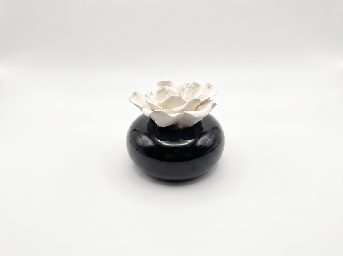 A small decorative ceramic object featuring a glossy black rounded base with a sculpted white flower rising from the top, photographed on a clean light gray studio background.