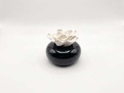 A small decorative ceramic object featuring a glossy black rounded base with a sculpted white flower rising from the top, photographed on a clean light gray studio background.