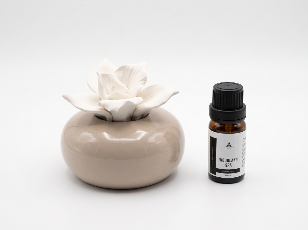 A ceramic diffuser with a glossy beige body and a white flower-shaped wax melt, shown next to a small amber glass bottle labeled 'Meadowland Spa' on a white background.