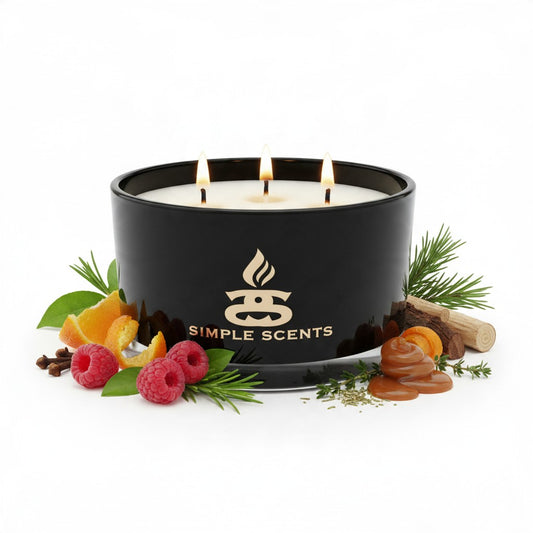 A black three-wick scented candle by Simple Scents with white wax, surrounded by decorative natural ingredients including raspberries, orange slices, pine needles, cinnamon, and a piece of wood on a white background.
