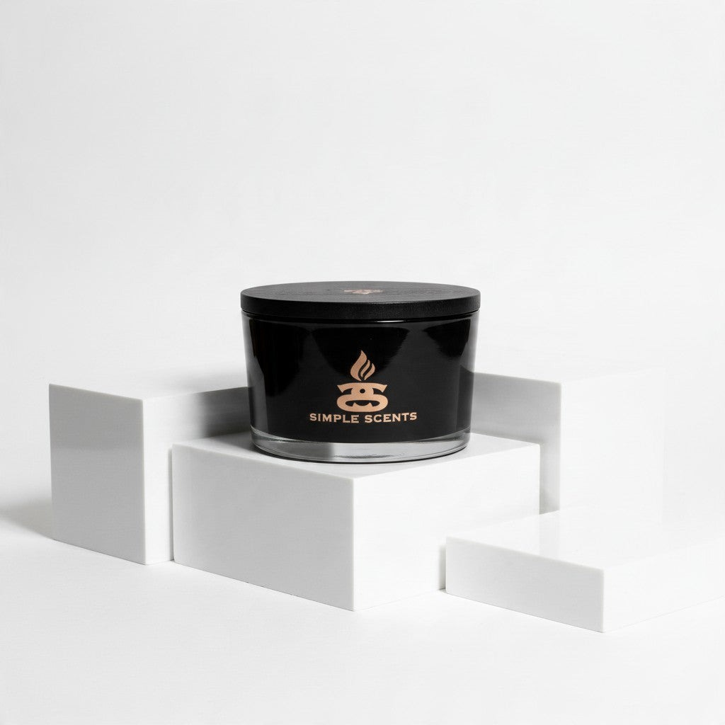 A black jar candle with a matching lid sits on a white geometric pedestal. The front of the jar is black with a gold logo and the words 'SIMPLE SCENTS'.