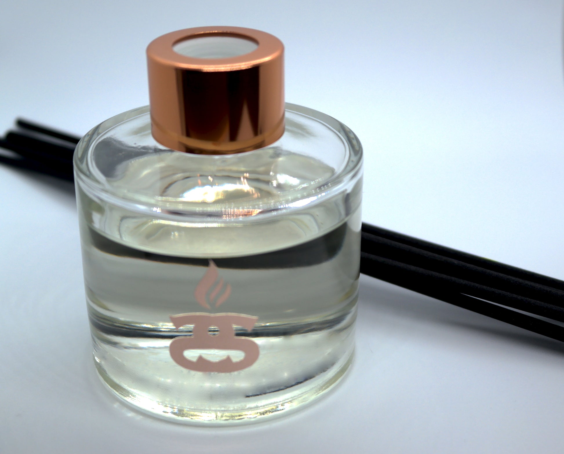 Simple Scents Excellence Reed Diffuser in 100ml glass squat bottle with rose gold cap lid and black fibre reeds laid horizontally behind